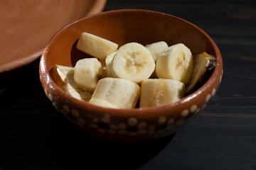 A view of a clay bowl of sliced banana pieces.