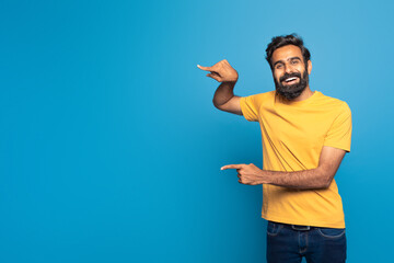 Indian man wearing a yellow shirt is pointing at an object or direction outside the frame of the...