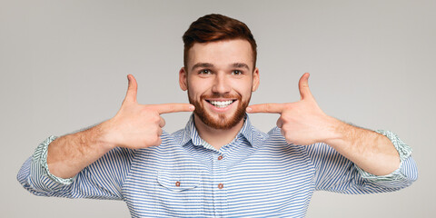 Dental hygiene. Young millennial man showing his beautiful smile and smooth teeth on beige background, panorama