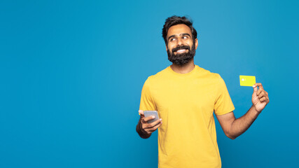 Indian man wearing a yellow shirt is seen holding a yellow card in one hand and a cell phone in the...