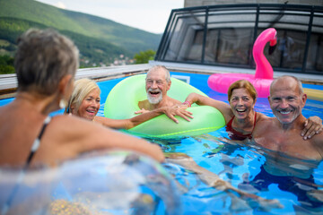 Group of cheerful seniors shaving fun in pool jumping, swiming and lounging on floats. Elderly...