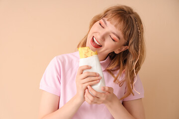 Young woman eating tasty sandwich wrap on beige background