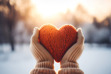 Hands in gloves holding heart shape knitted object on a blurred winter landscape background with trees
