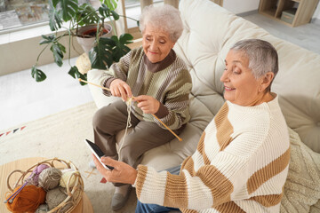 Senior female friends taking selfie while knitting on sofa at home