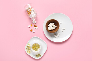 Plates, wooden bowl and bottle with different pills on pink background