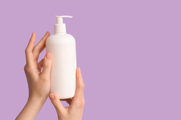 Female hands with bottle of natural cream on lilac background, closeup