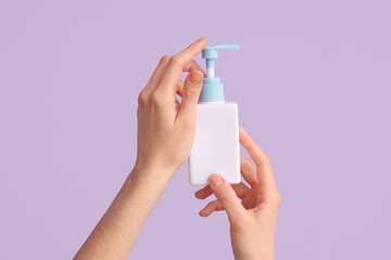 Female hands with bottle of natural cream against lilac background, closeup