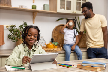 Cute little African American girl doing home work using digital tablet