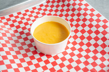 A view of a paper cup of nacho cheese dip.