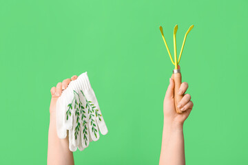 Female hands with gardening rake and gloves on green background, closeup
