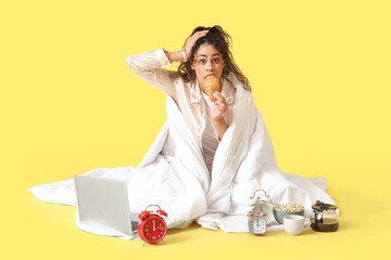 Hurrying young African-American woman with blanket, breakfast and alarm clocks on yellow background