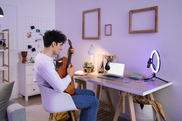 Male student playing guitar while streaming at home in evening