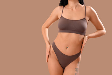 Beautiful young woman in brown underwear on beige background