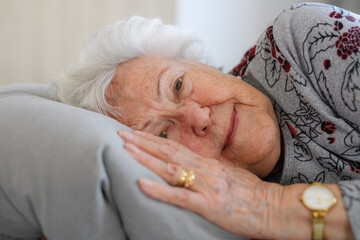 Senior woman lying in her bed alone, feeling anxious. Loneliness, social isolation of eldery woman.