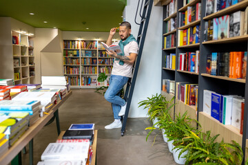 Young asian man standing near the book shelves and reading a book