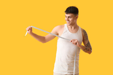 Young man with measuring tape on yellow background. Weight loss concept