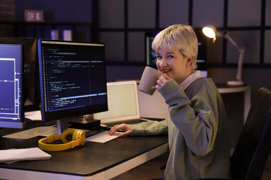 Female programmer drinking coffee in office at night