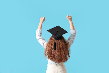 Female student in graduation hat on blue background, back view