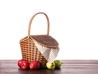 Wicker picnic basket with tasty food at brown wooden table isolated on white background