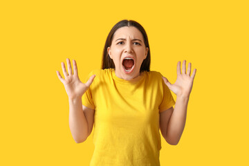 Angry young woman in yellow t-shirt screaming on color background