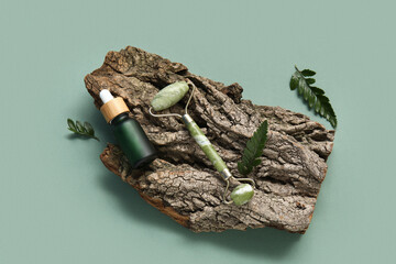 Tree bark with jade roller, serum and leaves on green background