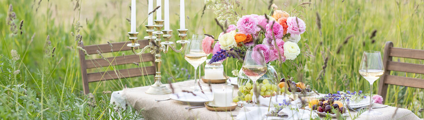 Surprise romantic date outdoors in a meadow. Elegant table with snacks and wine, chandelier with...