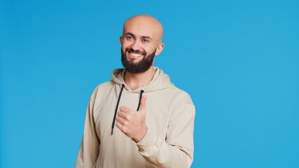 Arab male model gives a thumbs up in studio, expressing his satisfaction over blue background....