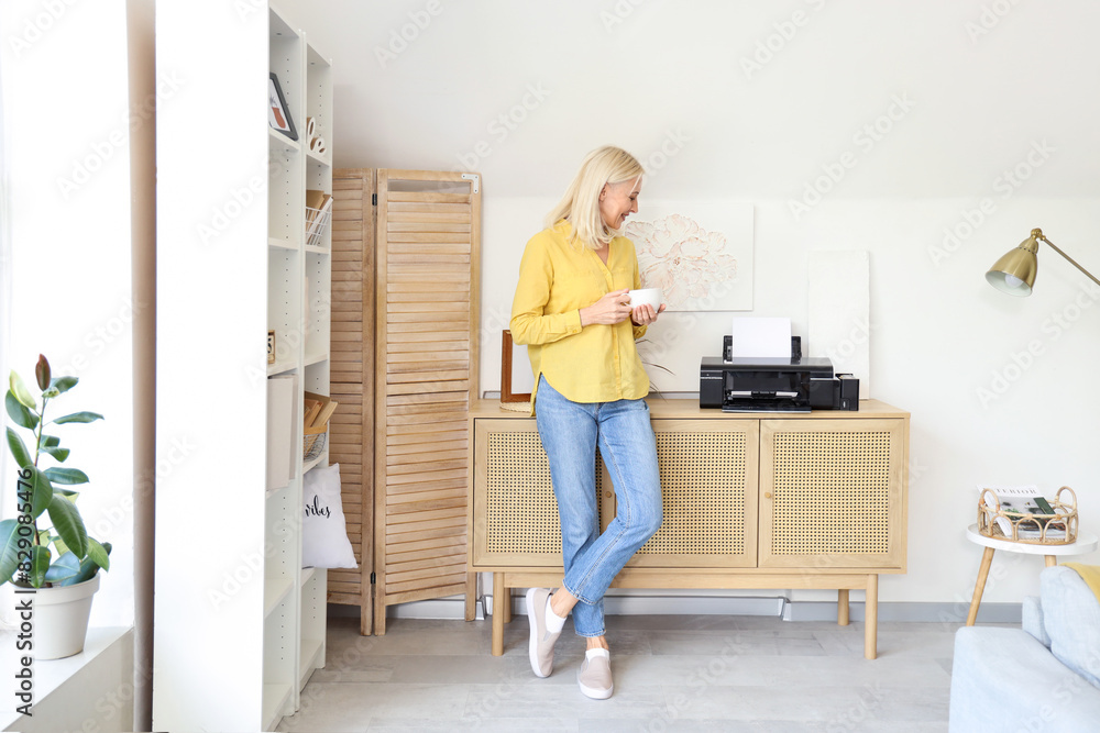 Canvas Prints Mature woman with cup of coffee and printer on commode at home