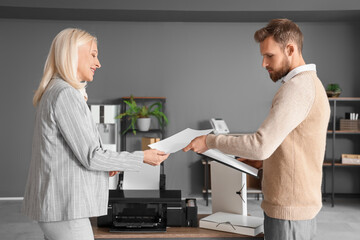 Mature businesswoman with her colleague printing document in office