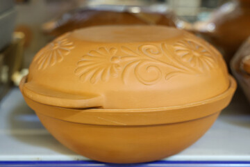 A large orange pot with a floral design sits on a shelf