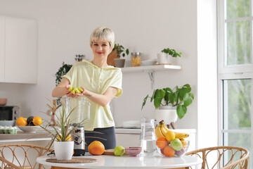 Sporty young woman putting cut apple into blender in kitchen