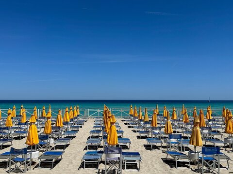 Rows of sun loungers, tables and closed parasols on beach, Mondello, Sicily, Italy