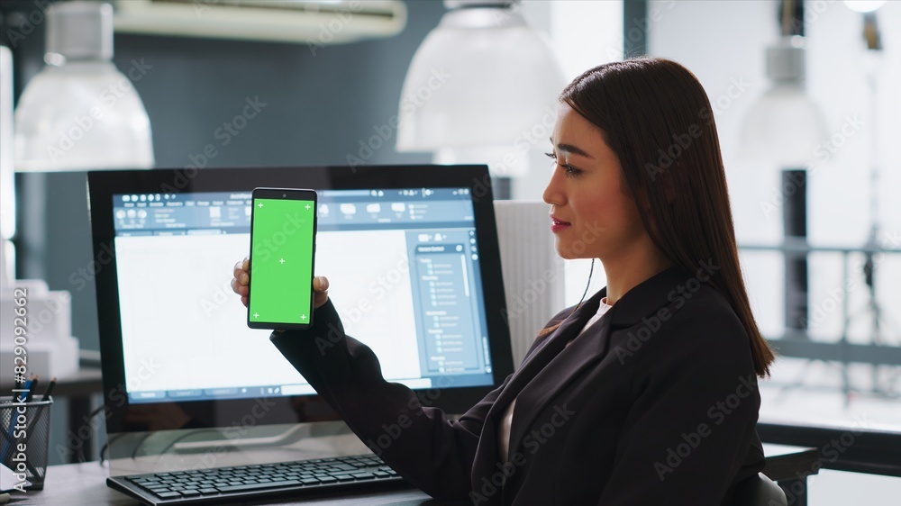 Poster developer shows mobile phone with greenscreen template, working in small business coworking space. e