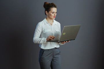 pensive elegant female worker using laptop isolated on gray