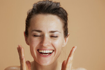 happy young woman with wet face washing isolated on beige