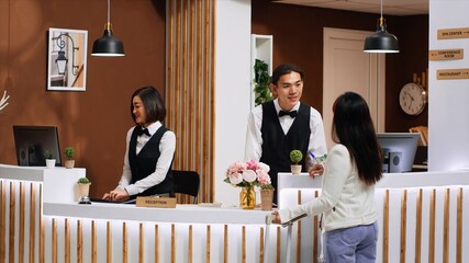 Front desk team staff welcoming hotel guest at reception, smiling and offering their concierge...