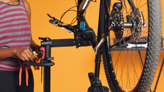 African american mechanic utilizing different tools to repair damaged bike handlebar grips, studio background. Employee using specialized gear to fix shifters and brake levers on bicycle, camera A