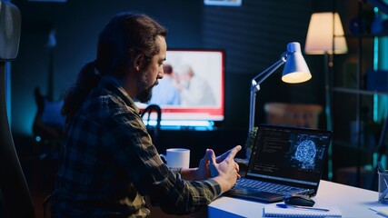 Programmer in living room office typing on keyboard, updating artificial intelligence neural...