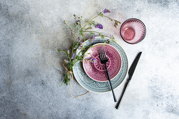 Overhead view of a rustic place setting with purple wildflowers on a grey background