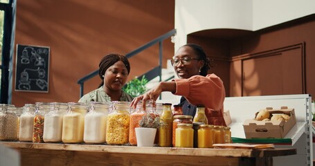 Vendor presents bio homemade sauces in reusable jars, recommending organic pantry supplies to...