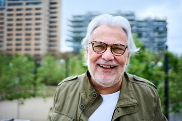 Portrait of happy mature Caucasian senior man standing outdoors with unfocused background garden...