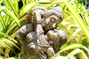 An ancient statue of lovers embraces serenity, surrounded by lush greenery in a tranquil setting
