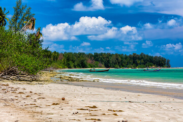 Palm tree fringed tropical sandy beach with  longtail boats at sea