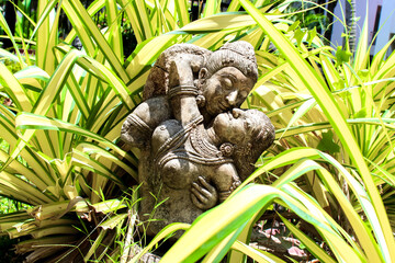 A stone sculpture captures the love between a couple in a vibrant garden setting with lush foliage