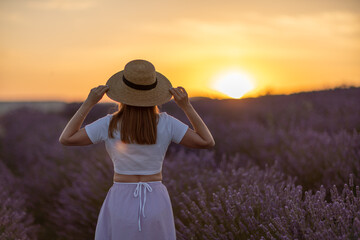 A woman wearing a straw hat stands in a field of lavender