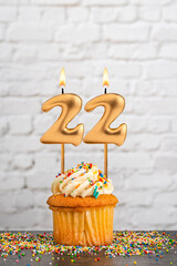 Golden birthday candle number 22 with cupcake - White block wall background
