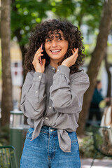 Happy Caucasian young woman having remote conversation communicate speaking by smartphone outdoors. Lady girl talking on phone unexpected good news gossip on city street. Town lifestyles. Vertical