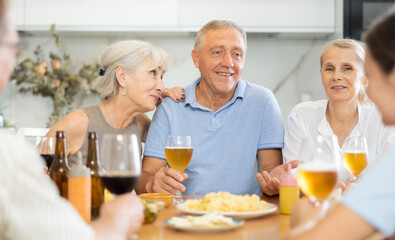Cheerful mature men and women having jolly conversation with goblets in hands during lunch time