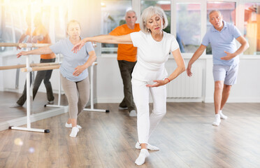 Obraz premium Positive mature woman practicing ballet positions standing in row with others in dance-studio
