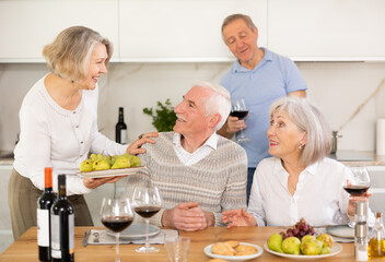 At the table, happy group of adults enjoy their holiday, drink red wine and talk together
